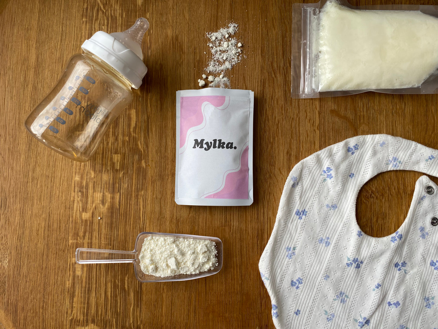 Baby bottle, Mylka powder package, scoop of powder, and bib on a wooden surface