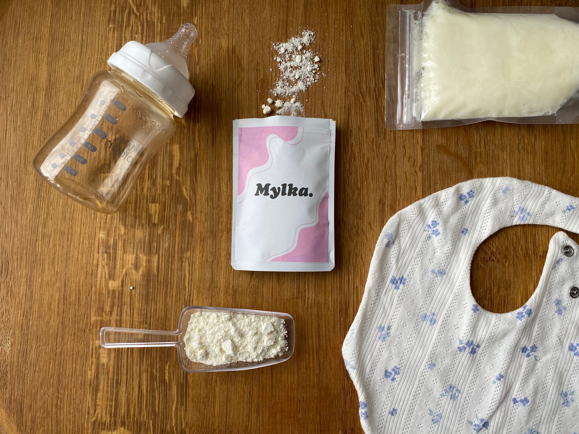 Baby bottle, Mylka powder package, scoop of powder, and bib on a wooden surface