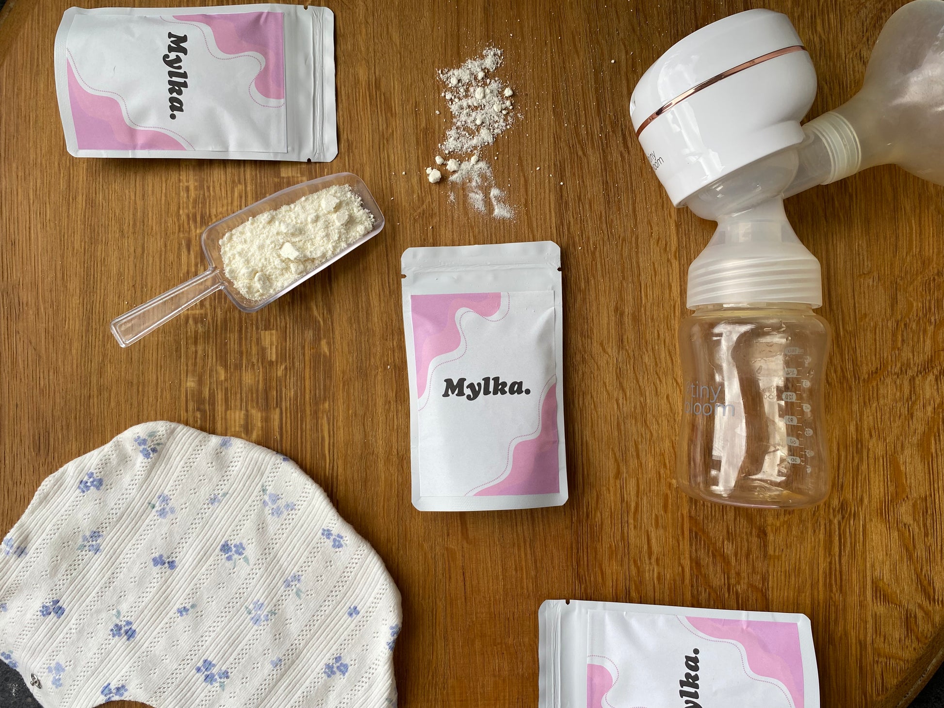 Mylka baby care products including a bottle, packaging, breast pump, and a scoop of powder on a wooden surface.