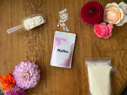 Mylka product styled on wooden surface with a scoop of powder and frozen breastmilk bag. 
