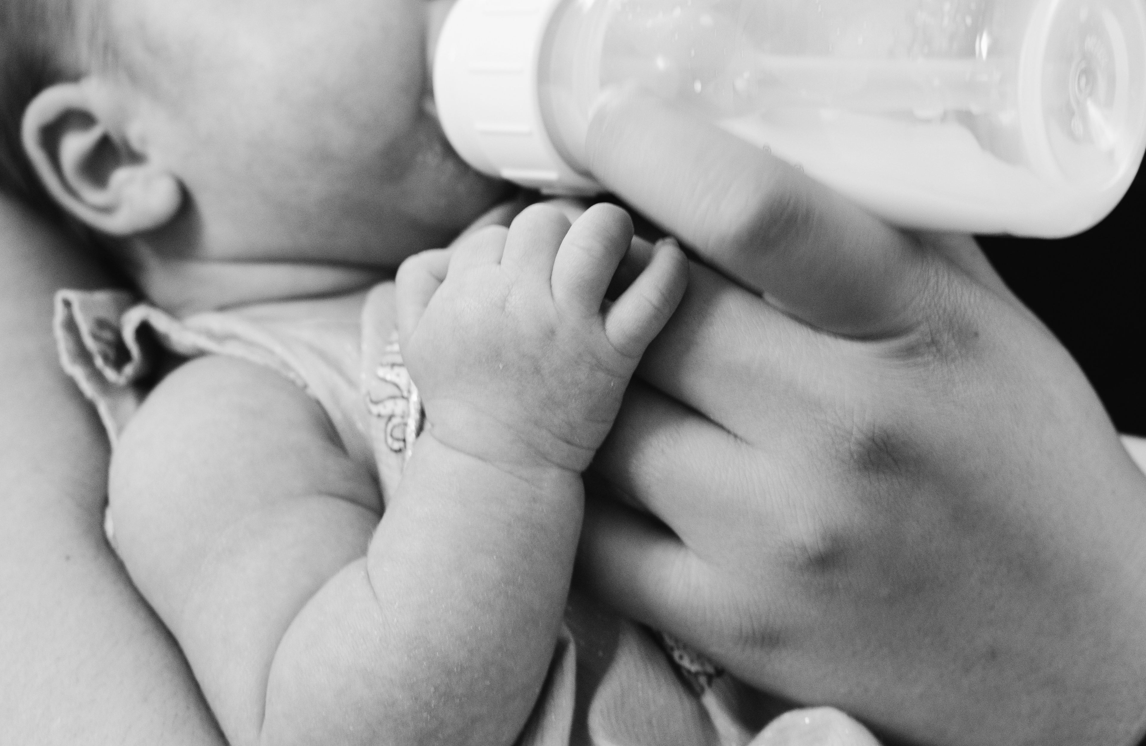 Black and white photo of a baby being fed from a bottle.